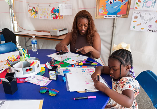 Woman and young girl sitting at a table drawing on paper